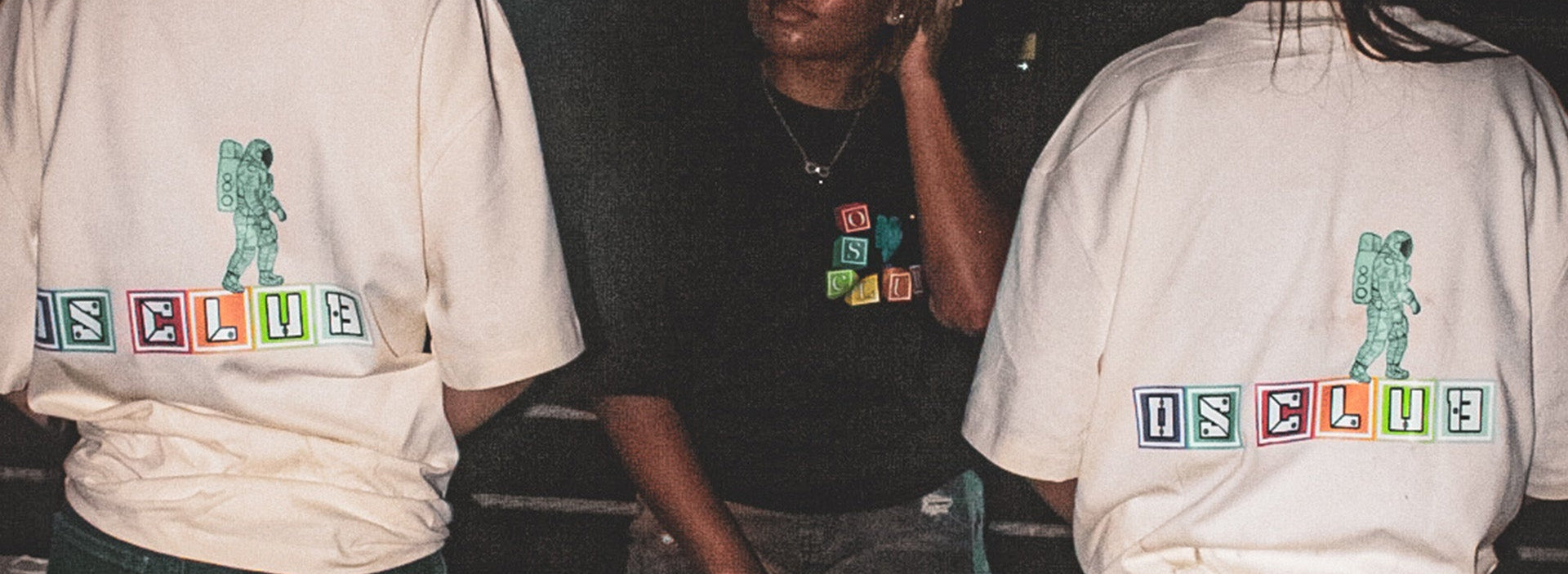 Three people wearing t-shirts with 'OS CLUB' design on a dark background